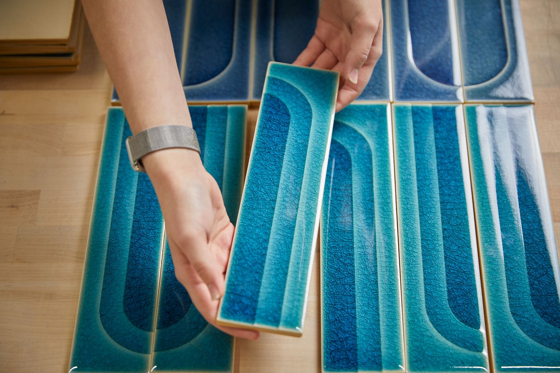 A person holding a blue tile created by KOHLER WasteLAB shows the varying color gradients and crackle designs in an arch pattern.