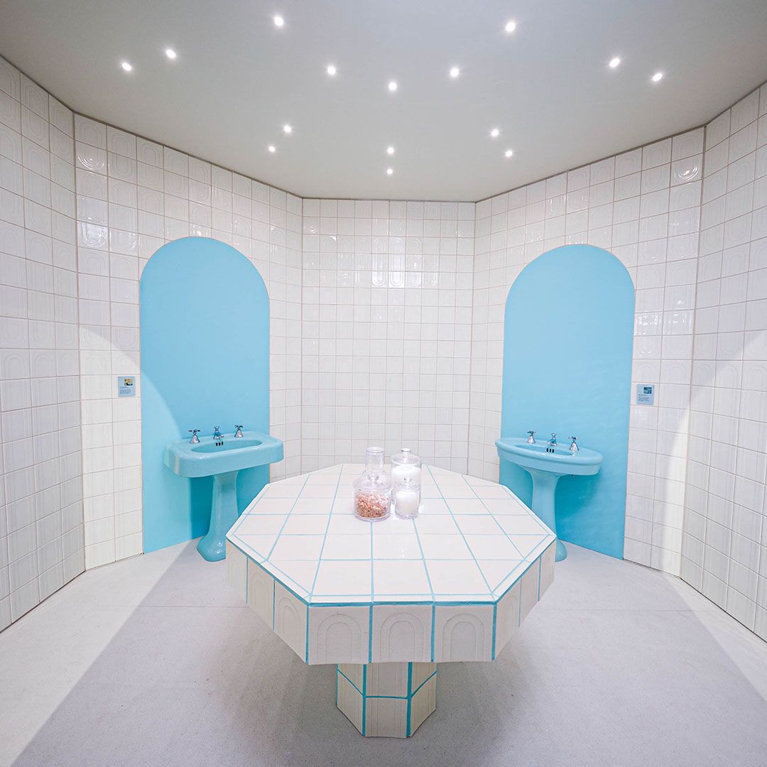 The interior of the warm room at the Nada Debs Design/Miami installation showing tiles in bone finish and pedestal sinks in heritage color spring green.