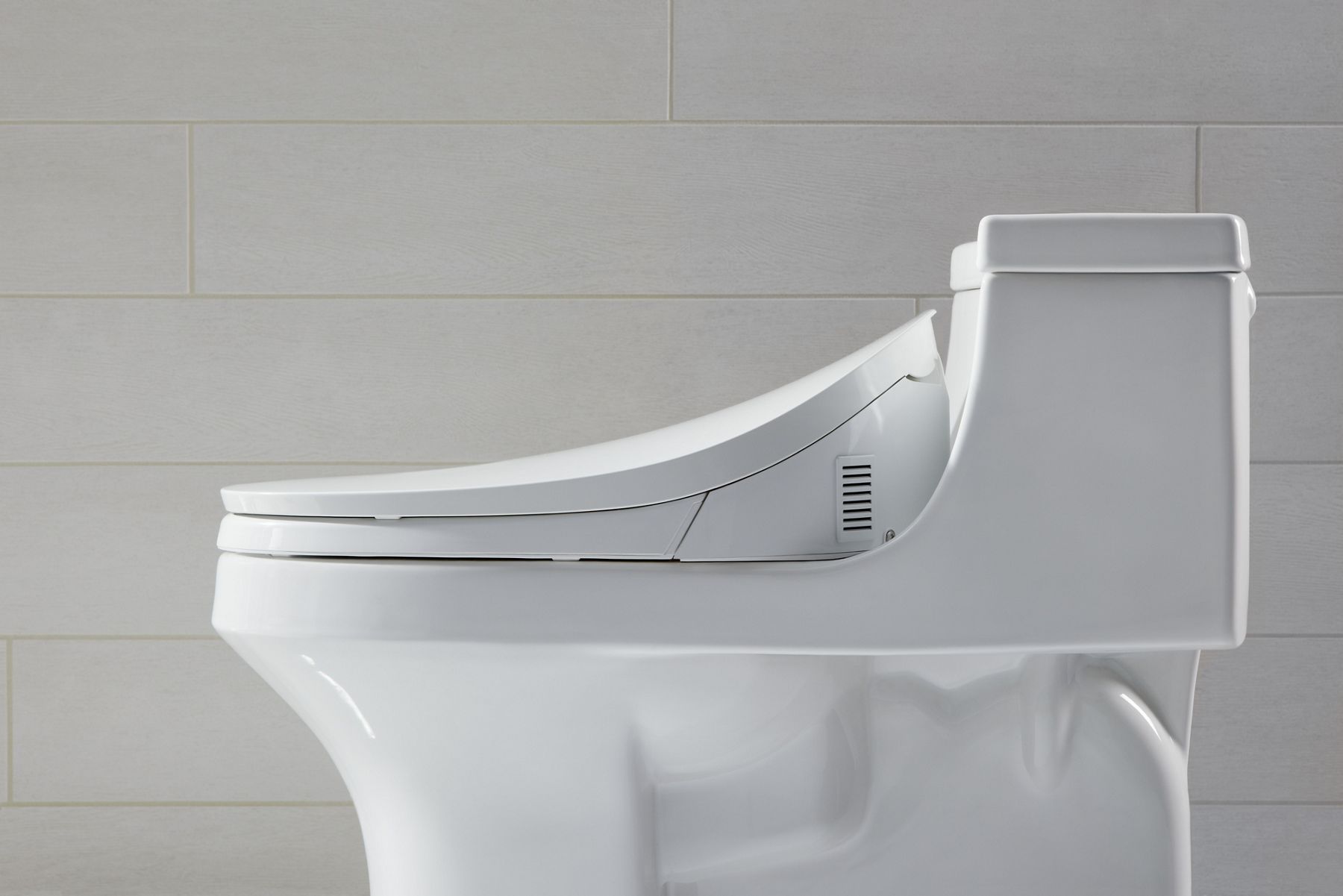 A white KOHLER elongated toilet with bidet seat, profile view.