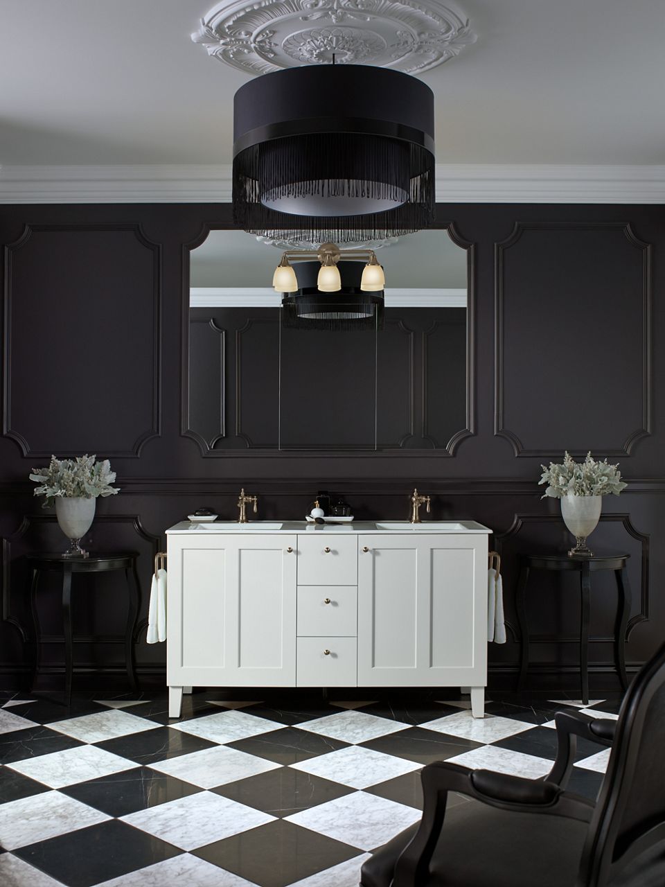 A white KOHLER vanity with a mirror above it reflect a chandelier in a black and white bathroom