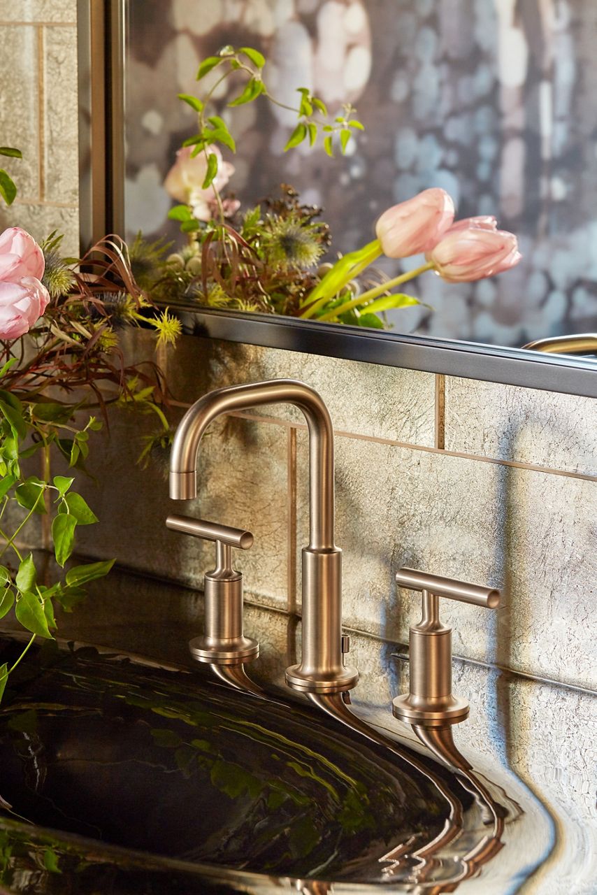 A Purist widespread faucet in brushed bronze next to a bouquet of pink tulips on a glossy vanity top.