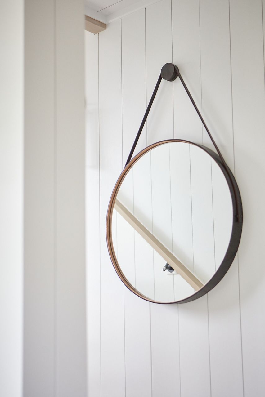 Un miroir rond est suspendu dans une cage d’escalier avec des murs en tableau blanc.