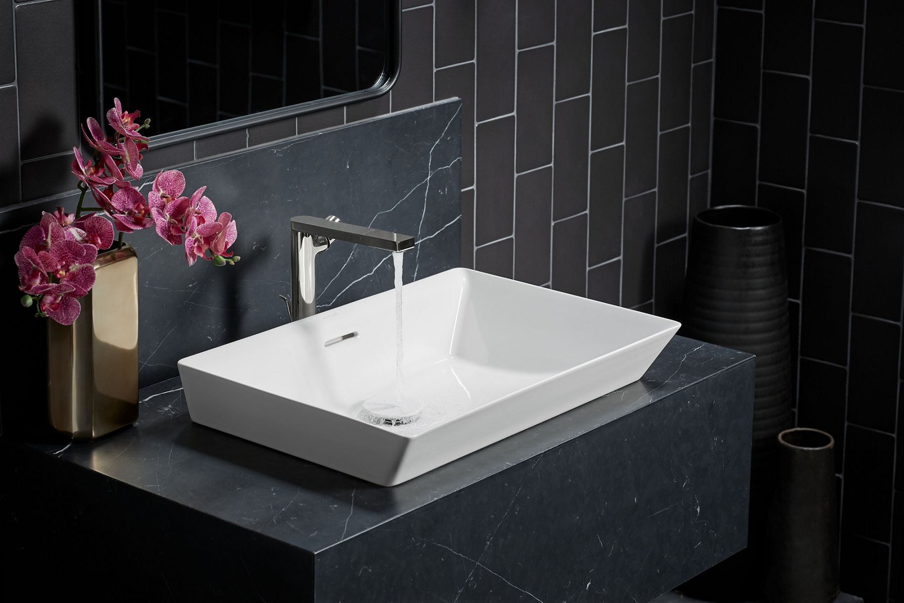 Water flows from a KOHLER single lever handle faucet into a white rectangle vessel sink mounted on a dark gray vanity.