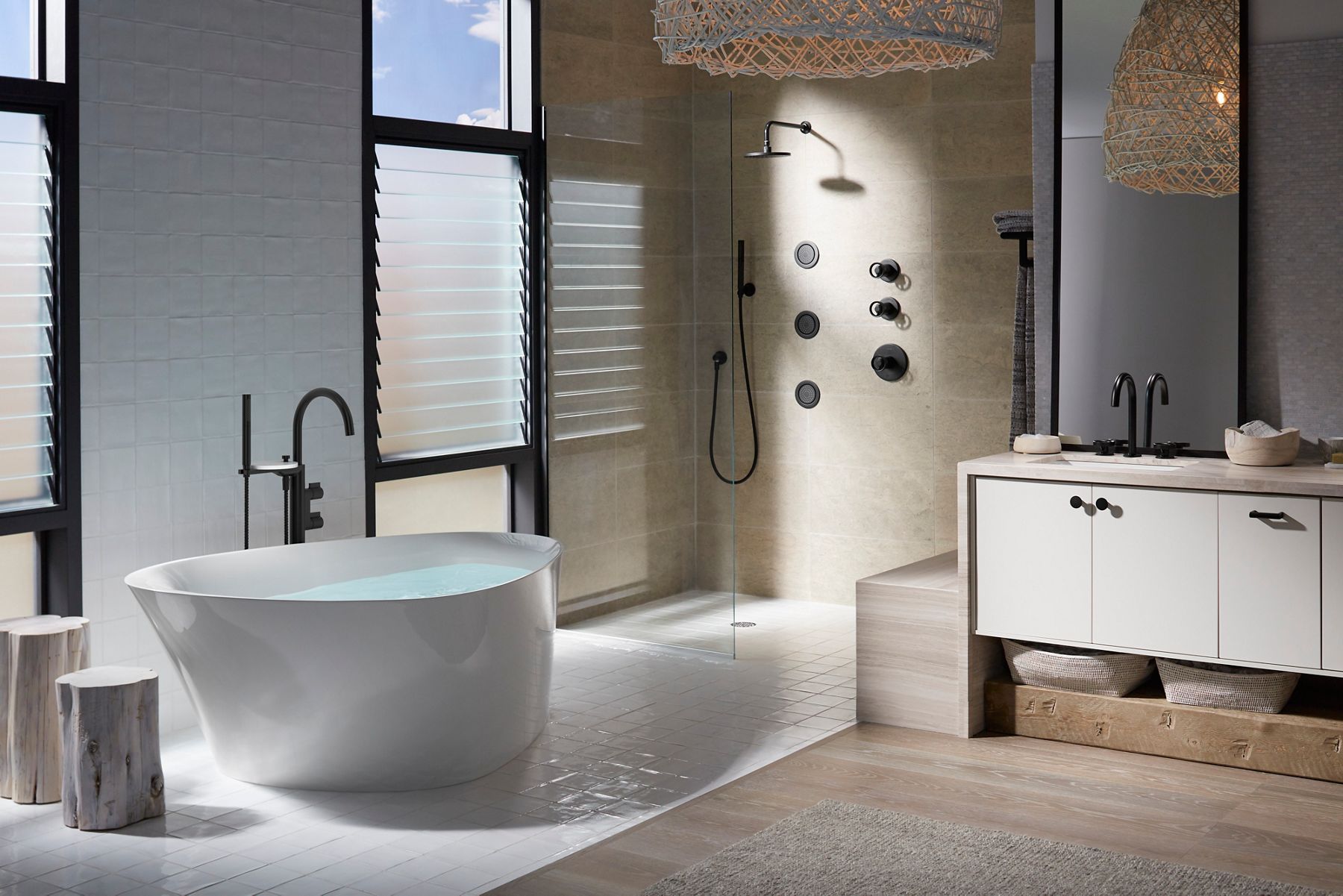 Une salle de bains sombre, éclairée par les stores de la fenêtre qui projettent des ombres fortes sur une baignoire autoportante, une douche ouverte et un espace beauté.