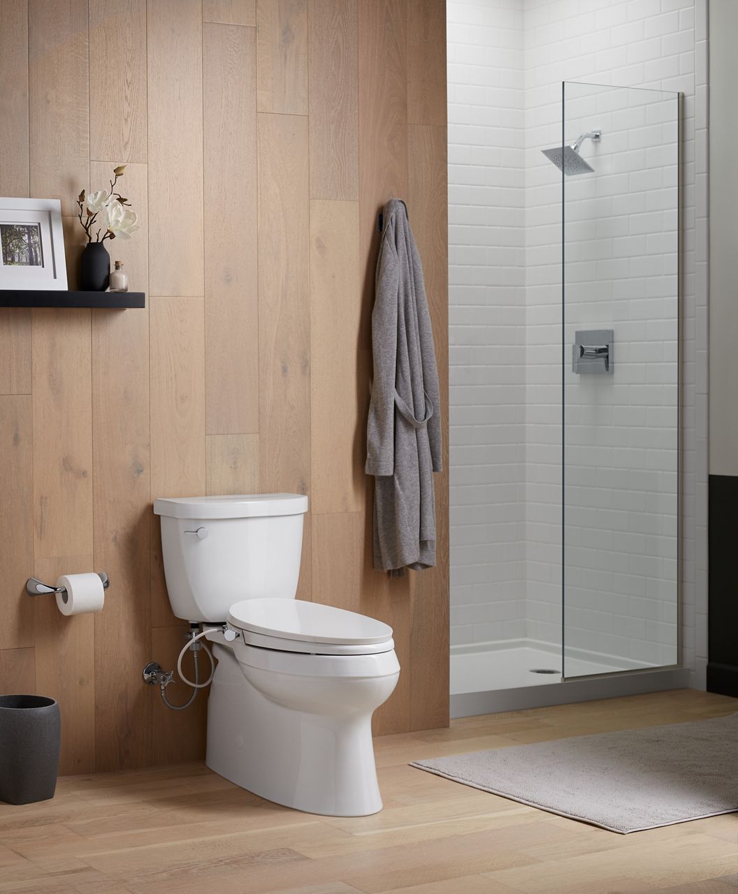 A white KOHLER elongated toilet with bidet seat in a bathroom with brown paneled walls.