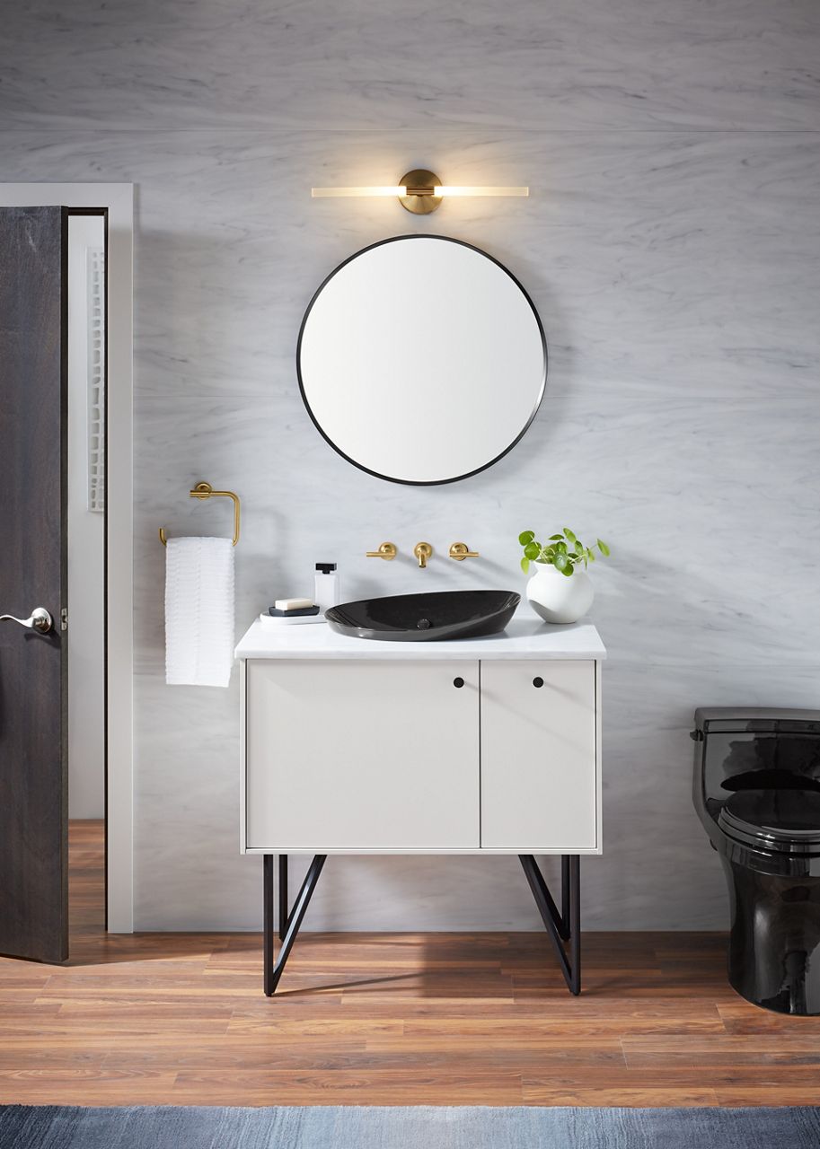 A round mirror hangs above a white vanity with black KOHLER Veil vessel sink and a wall mounted widespread lever handle faucets.