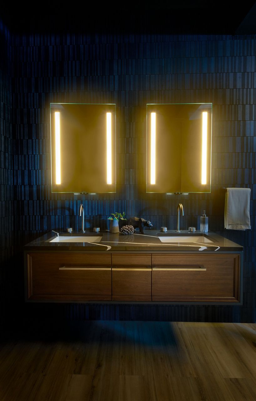 A bathroom with double vanity with undermount sinks, blue tiled wall, and two KOHLER lighted mirrors hung side by side.