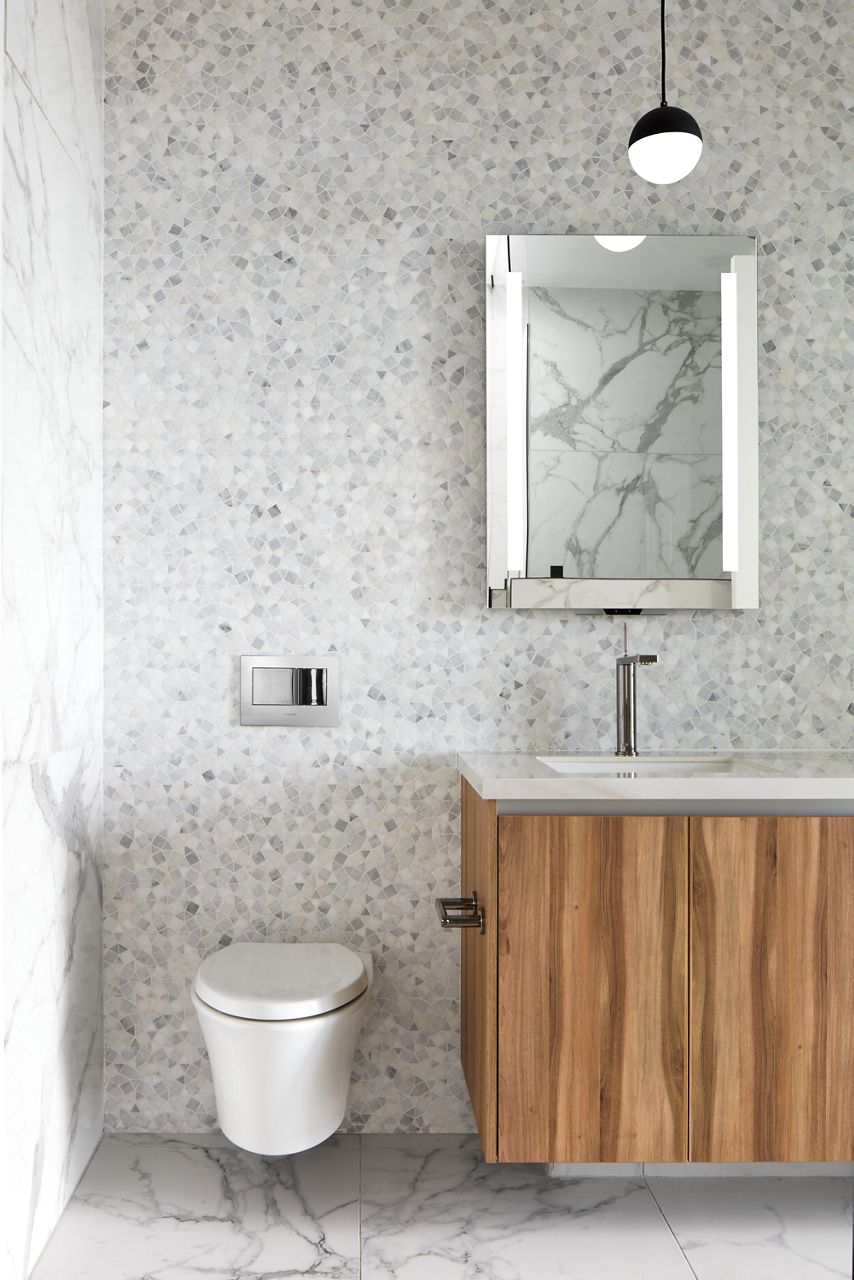 Image modern bathroom with textured walls and marbled flooring with view of wall-mounted intelligent toilet adjacent to bathroom sink and mirror.