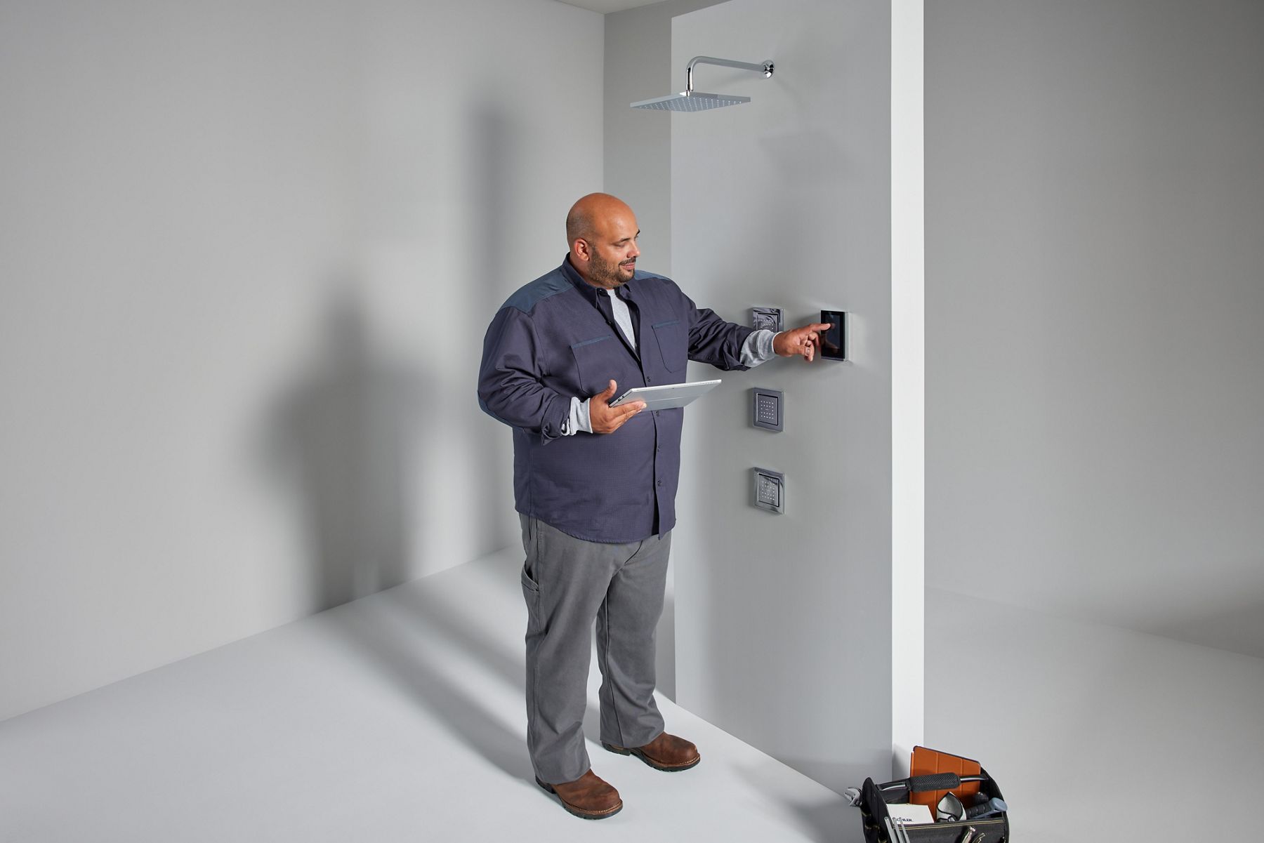 A contractor holding a tablet sets up a wall mount control system for a digital shower.