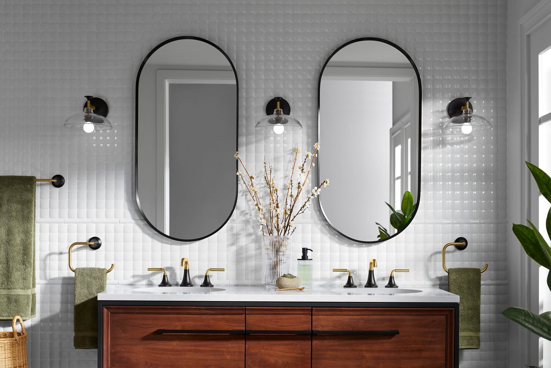 A white bathroom with two capsule mirrors, three sconces, and a double vanity with white top and two-toned, widespread bathroom sink faucets.