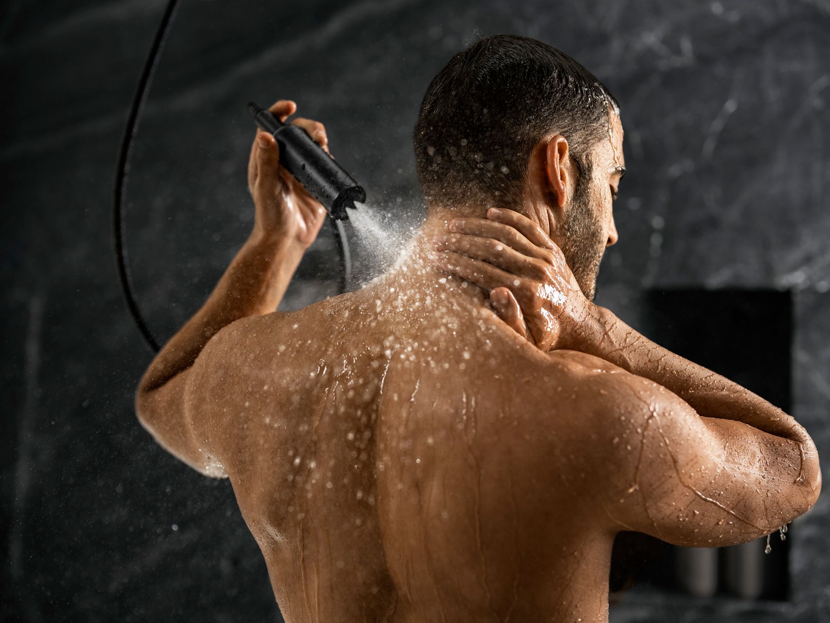 Un homme utilisant une douchette pour vaporiser de l’eau sur l’arrière de son cou.