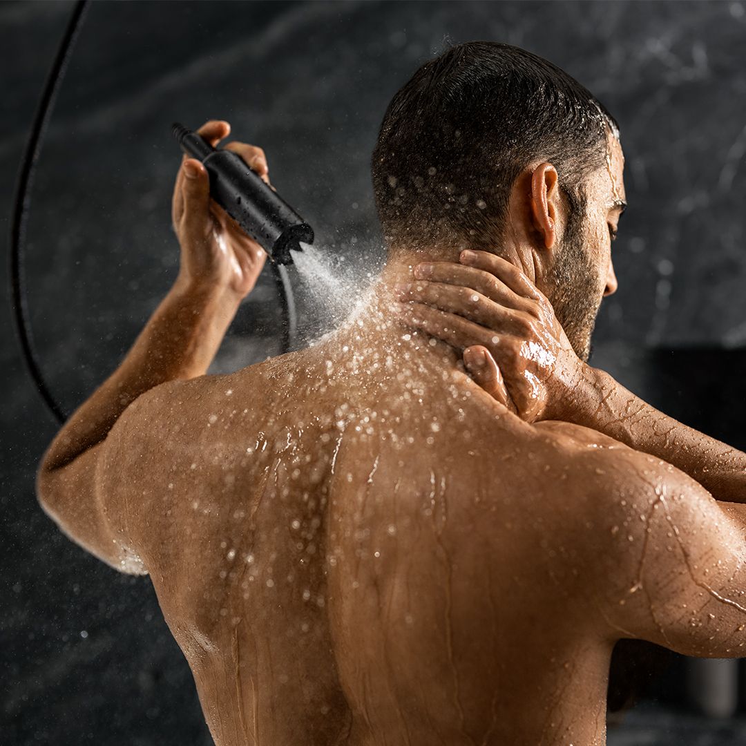 A man rinsing his back with a handheld showerhead.