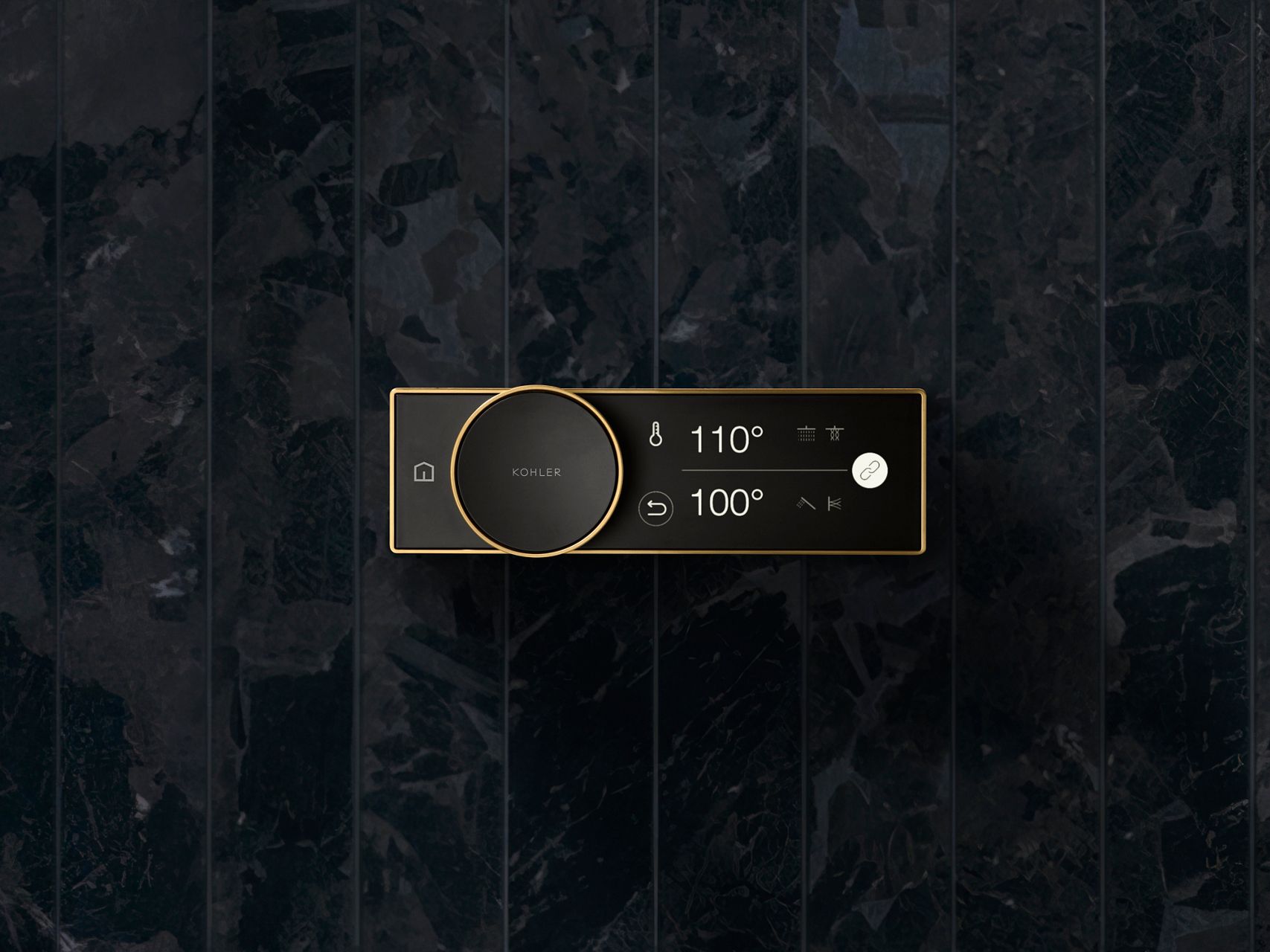 An Anthem digital shower control in black with brass trim on a dark gray stone wall.