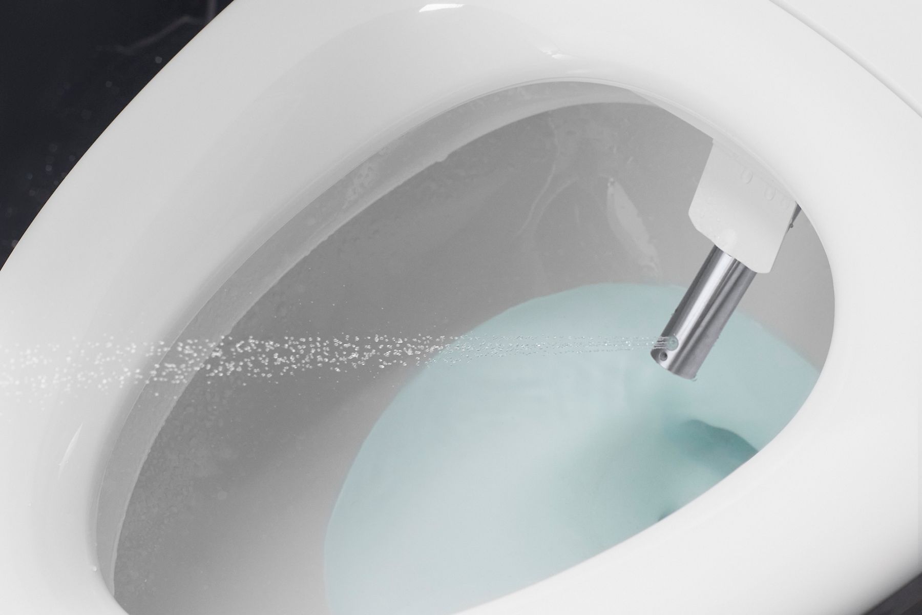 Close-up of a bidet nozzle spraying water inside a toilet bowl, emphasizing cleanliness.