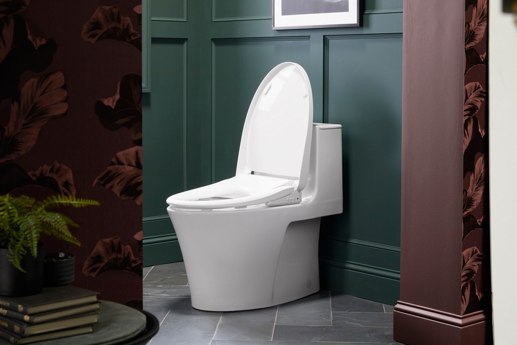 Modern white toilet with a high-tech design and sleek profile set against a dark green wall.