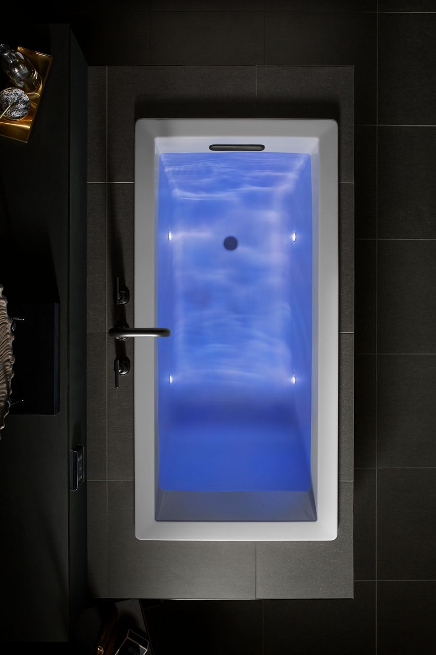 Overhead view of a filled white bathtub with violet lights projecting throughout the water.