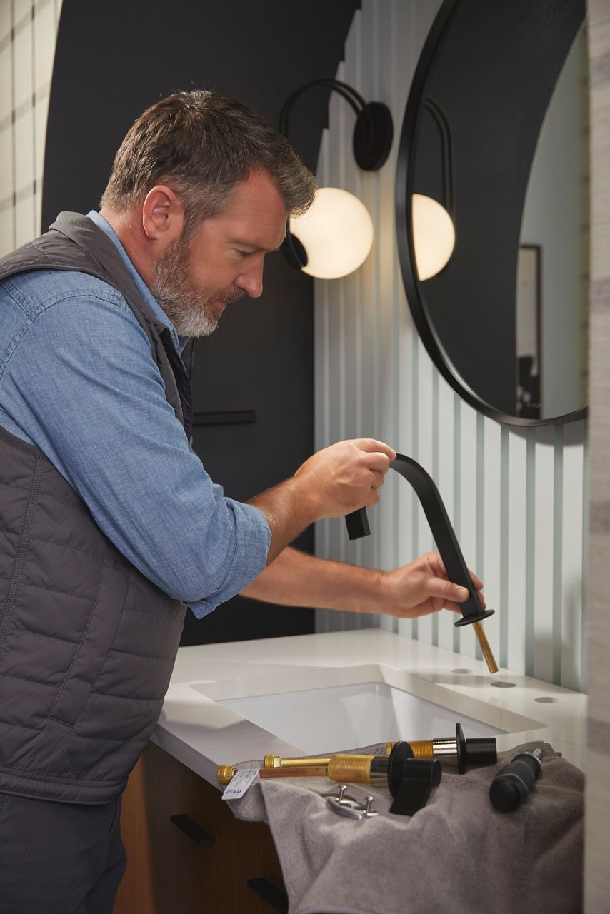 Person installing matte black and brass faucet on a bathroom sink.