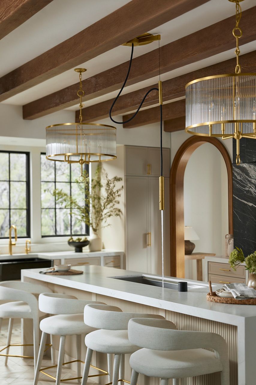 A Purist Suspend faucet hanging from the ceiling in a kitchen with natural wood grain cabinets and a white farmhouse sink. 