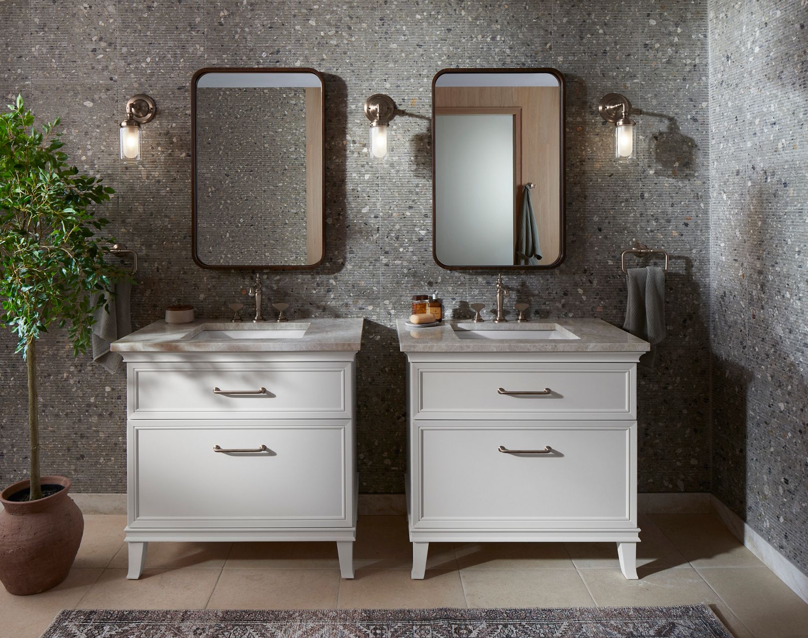 Une salle de bain bien éclairée avec deux lavabos, de grands miroirs avec cadre, des appliques murales et un dosseret en carrelage texturé.