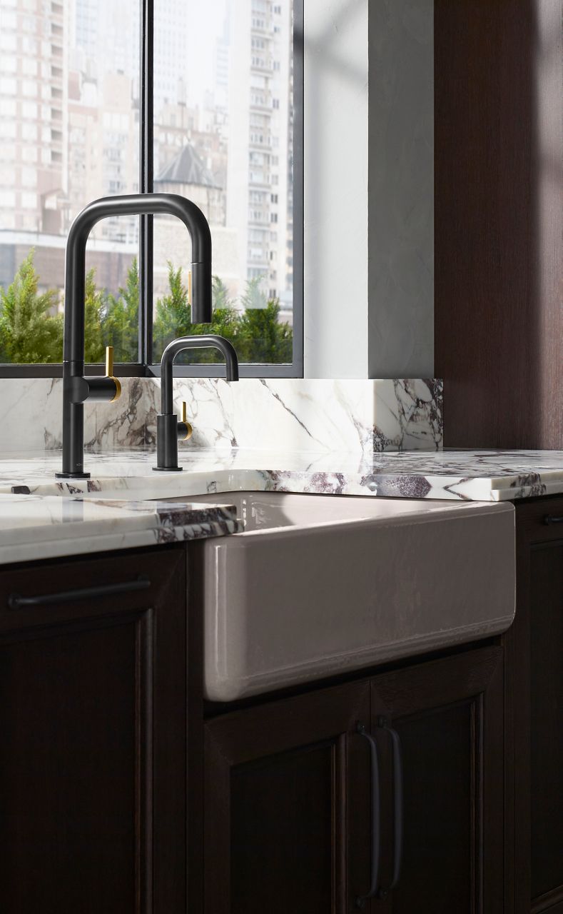 Dark kitchen sink and matte black faucet beside a window with city views and a marble countertop.
