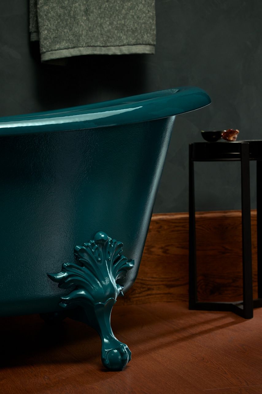 Freestanding teal clawfoot bathtub on a wooden floor in a dimly lit bathroom.