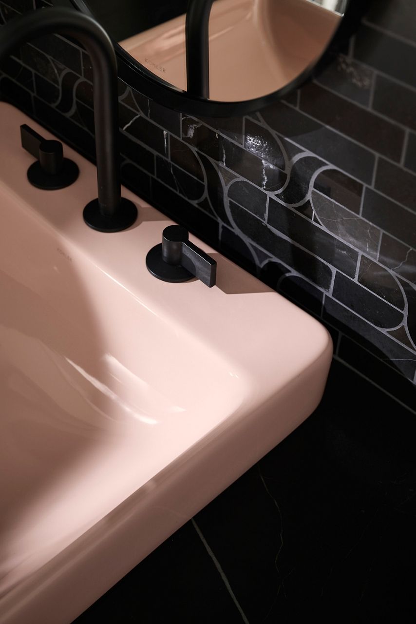 Soft pink sink with matte black faucet and dark tiled backsplash featuring a subtle abstract pattern.