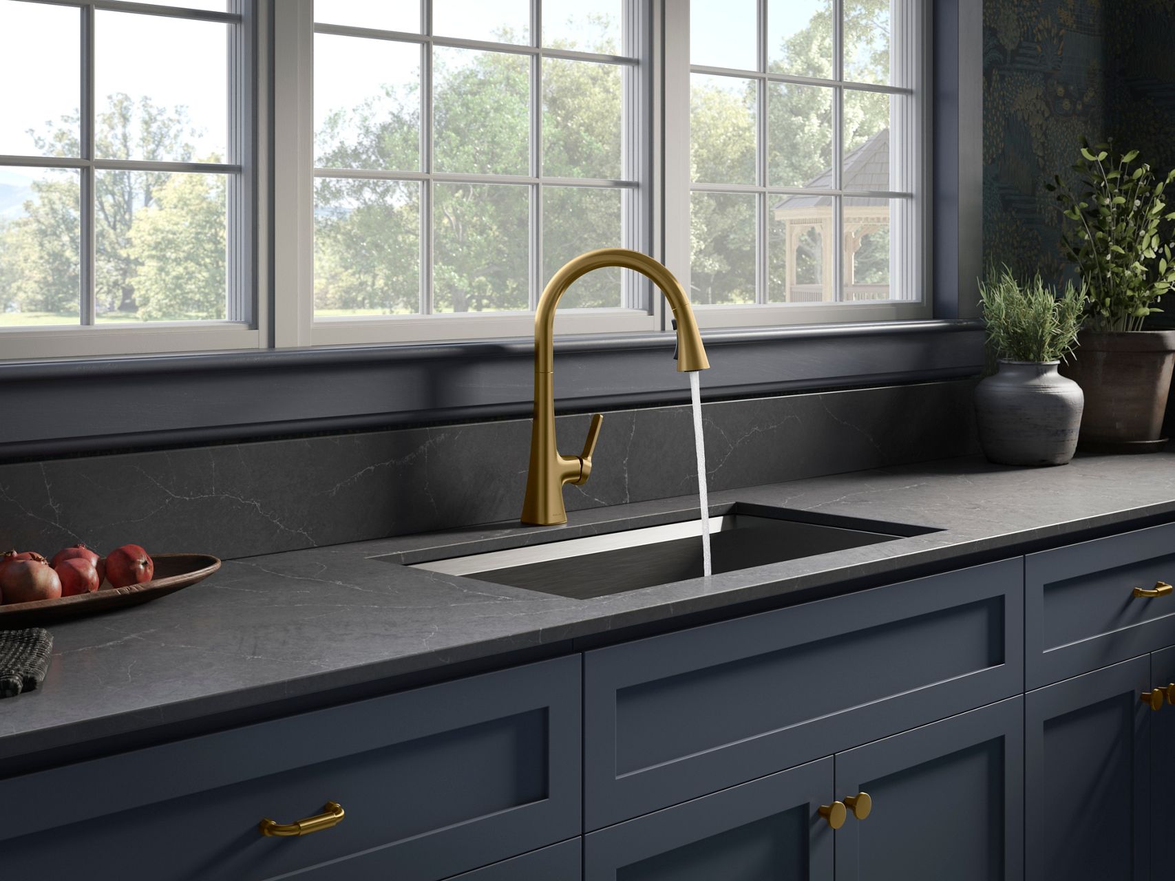 Modern kitchen featuring a matte black countertop with an integrated dark sink, paired with a brushed brass faucet beneath large grid windows. Navy blue cabinetry with brass hardware completes the space.