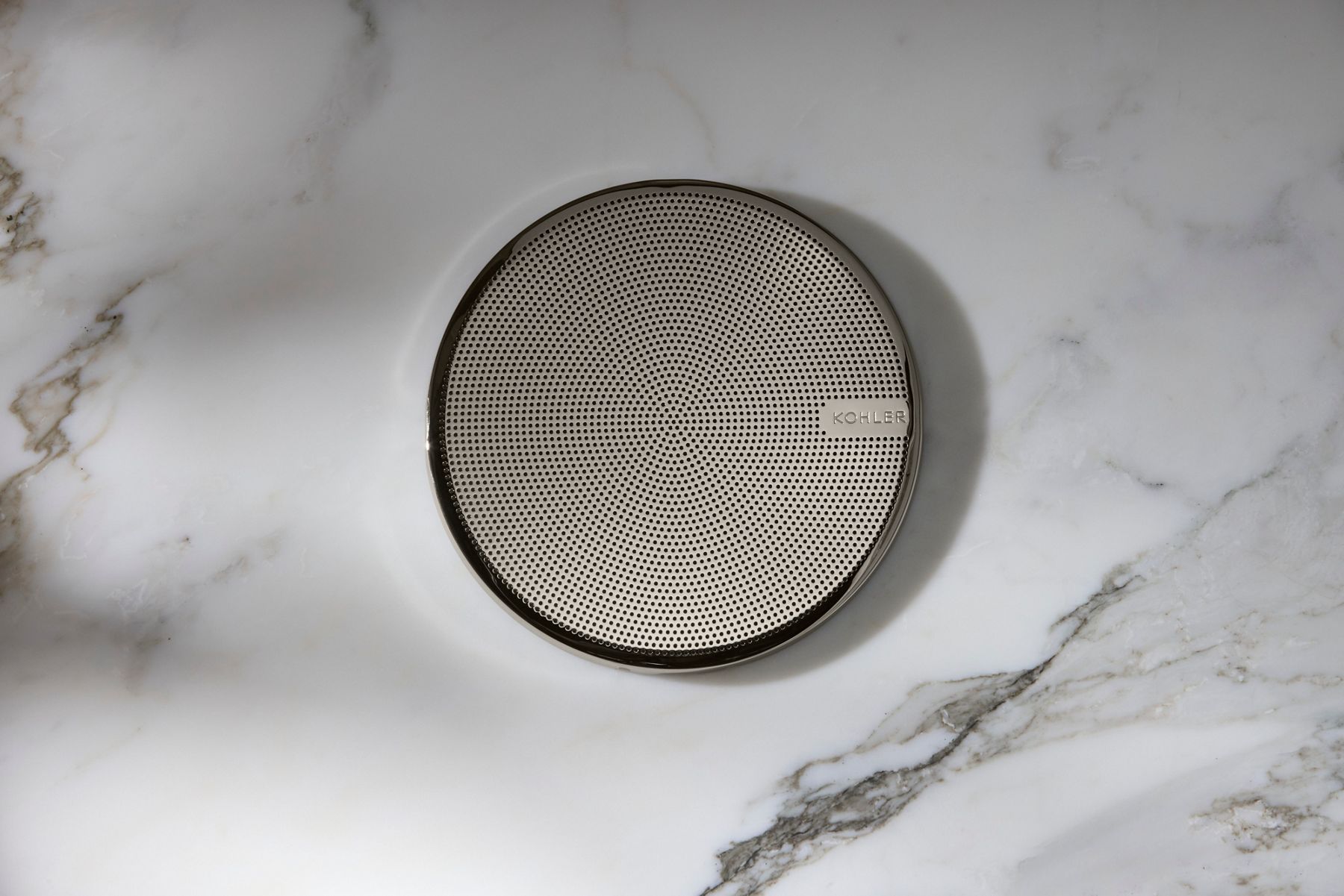 Round SoundTile shower speaker mounted on a white marble wall with water resistant design.