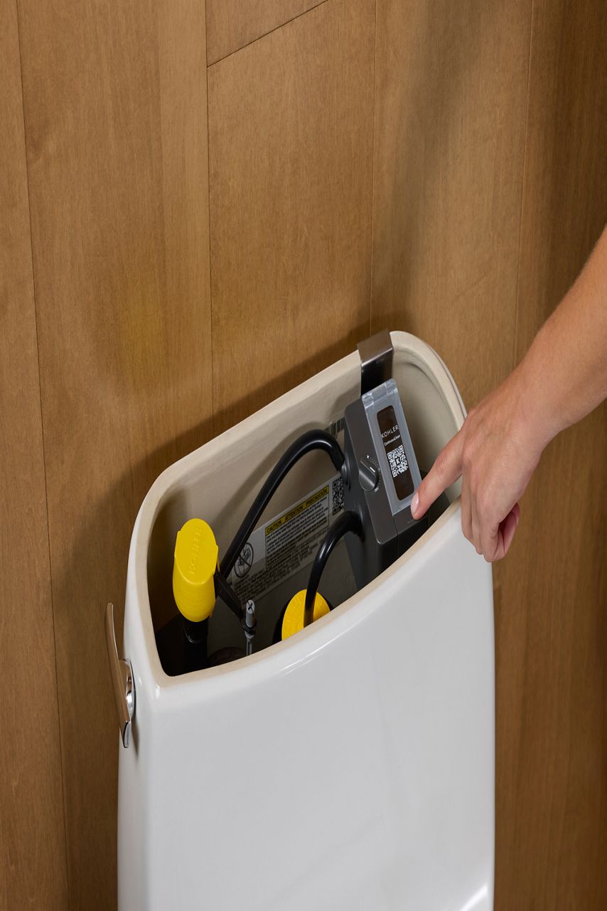 Personne manipulant un composant du réservoir de toilette intelligente de Kohler, comportant un code QR pour l’installation ou le dépannage.