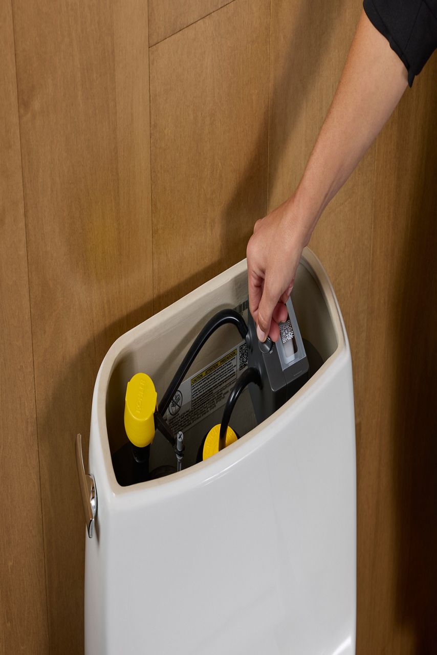 Une personne ajuste un composant à l’intérieur du réservoir d’une toilette intelligente Kohler pour la personnaliser ou l’entretenir.