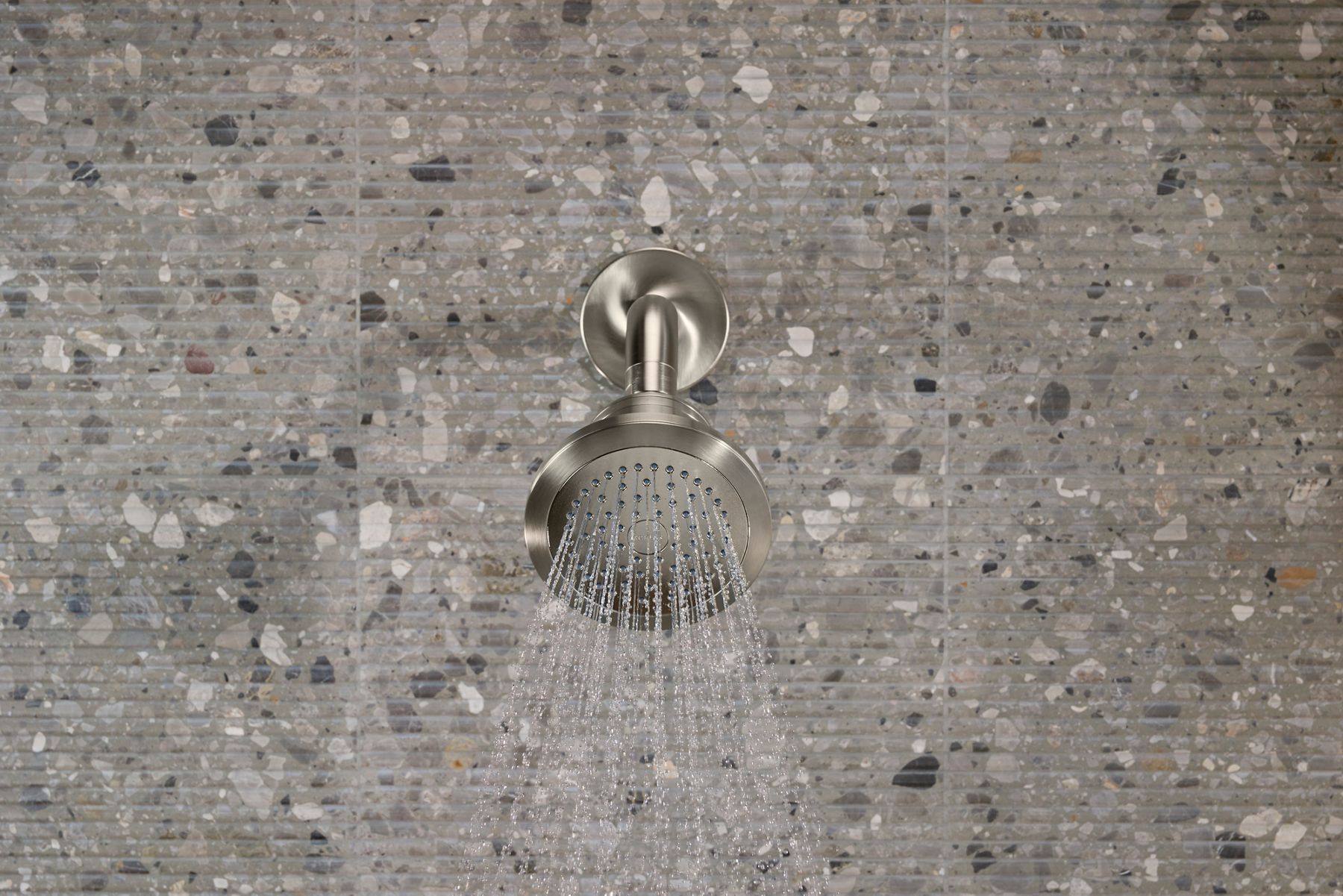 Cinq filtered showerhead mounted on a tiled wall, spraying water downward in a steady stream.