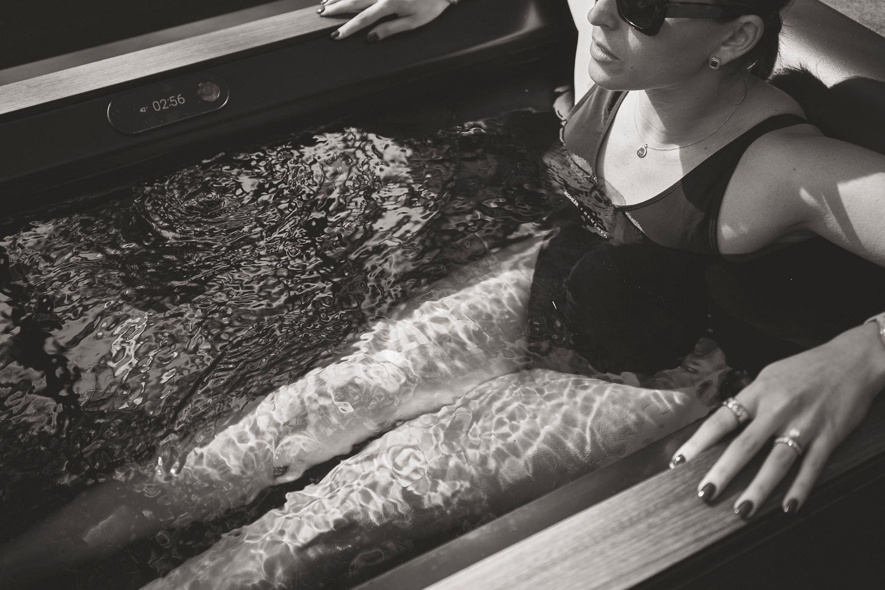 Close-up of a woman relaxing in a spa setting, with hands gently resting on her legs covered in patterned water or treatment