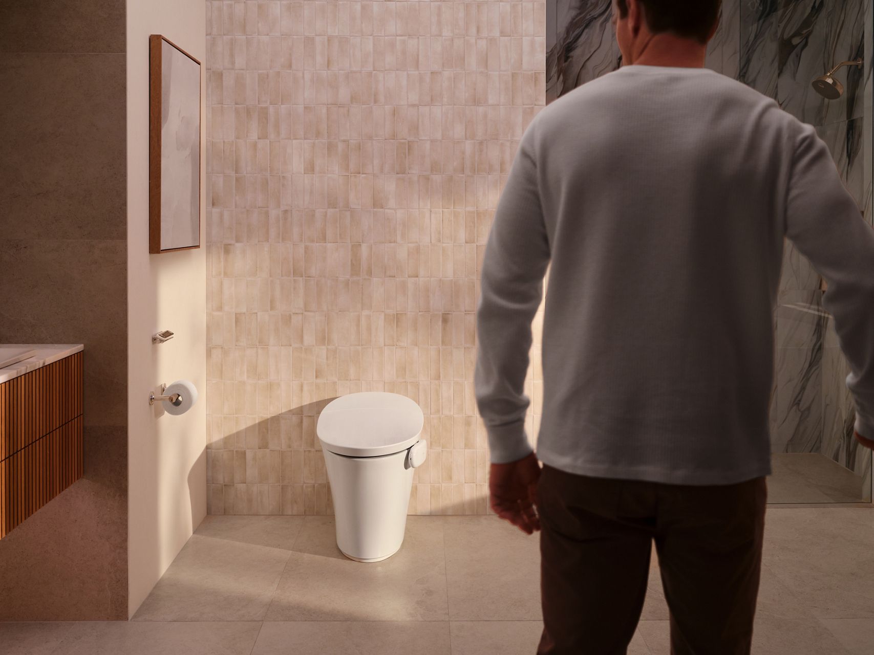 Person approaching a toilet equipped with the Kohler Health Dekoda device, representing blood presence monitoring through the Kohler Health app.