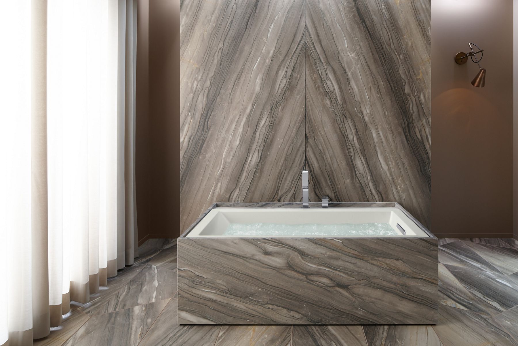 An undermount bathtub filled with moving water in a bathroom with a dramatic taupe colored stone enclosure, wall and floor.