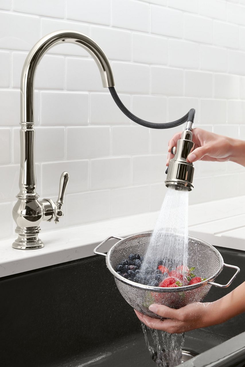 A colander full of strawberries and blueberries over a sink as the spout of a faucet gently washes the fruit using the BerrySoft spray.