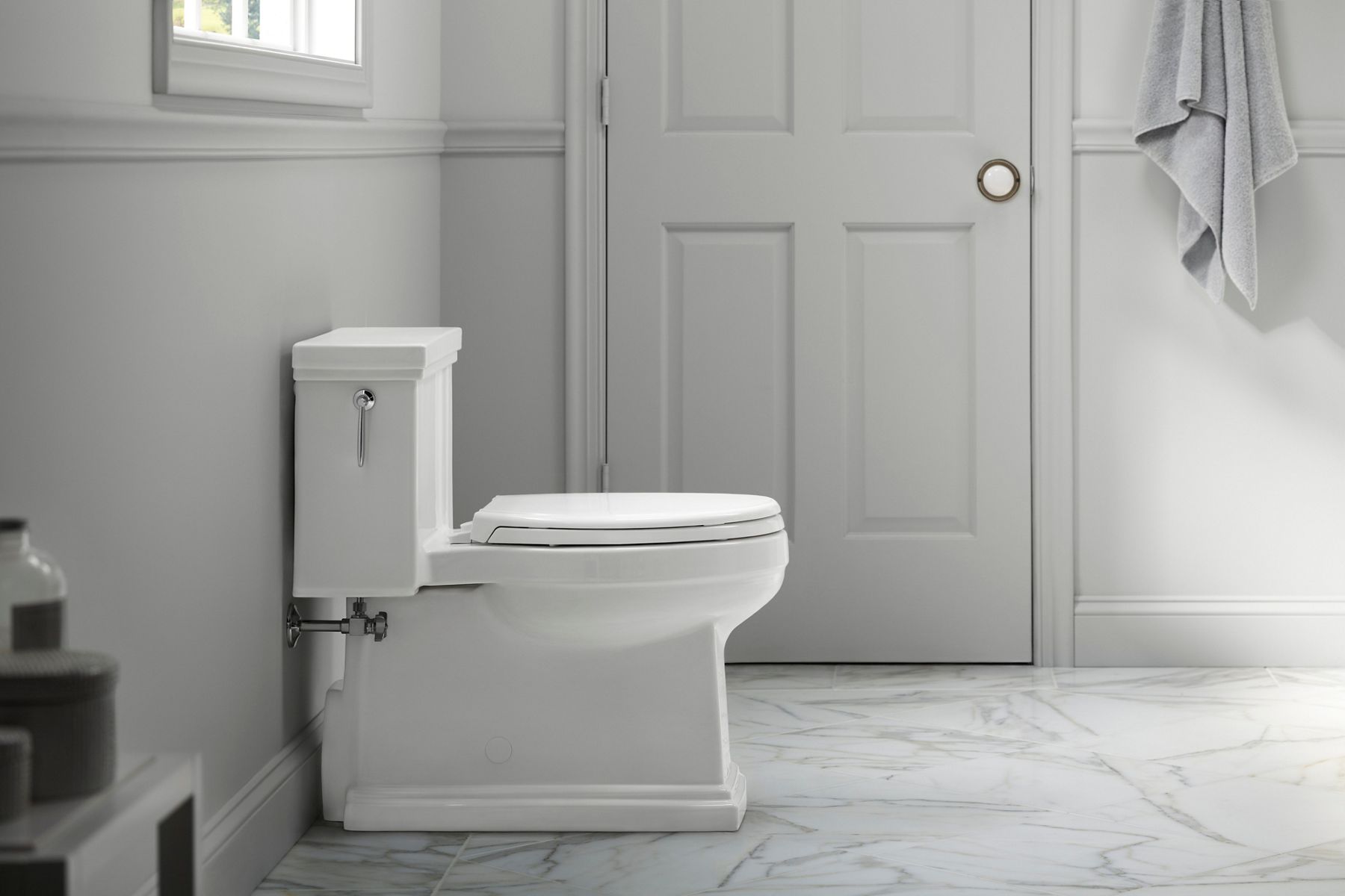Une toilette à siphon dissimulé Tresham de KOHLER installée dans une salle de bain aux planchers de marbre et aux murs gris.