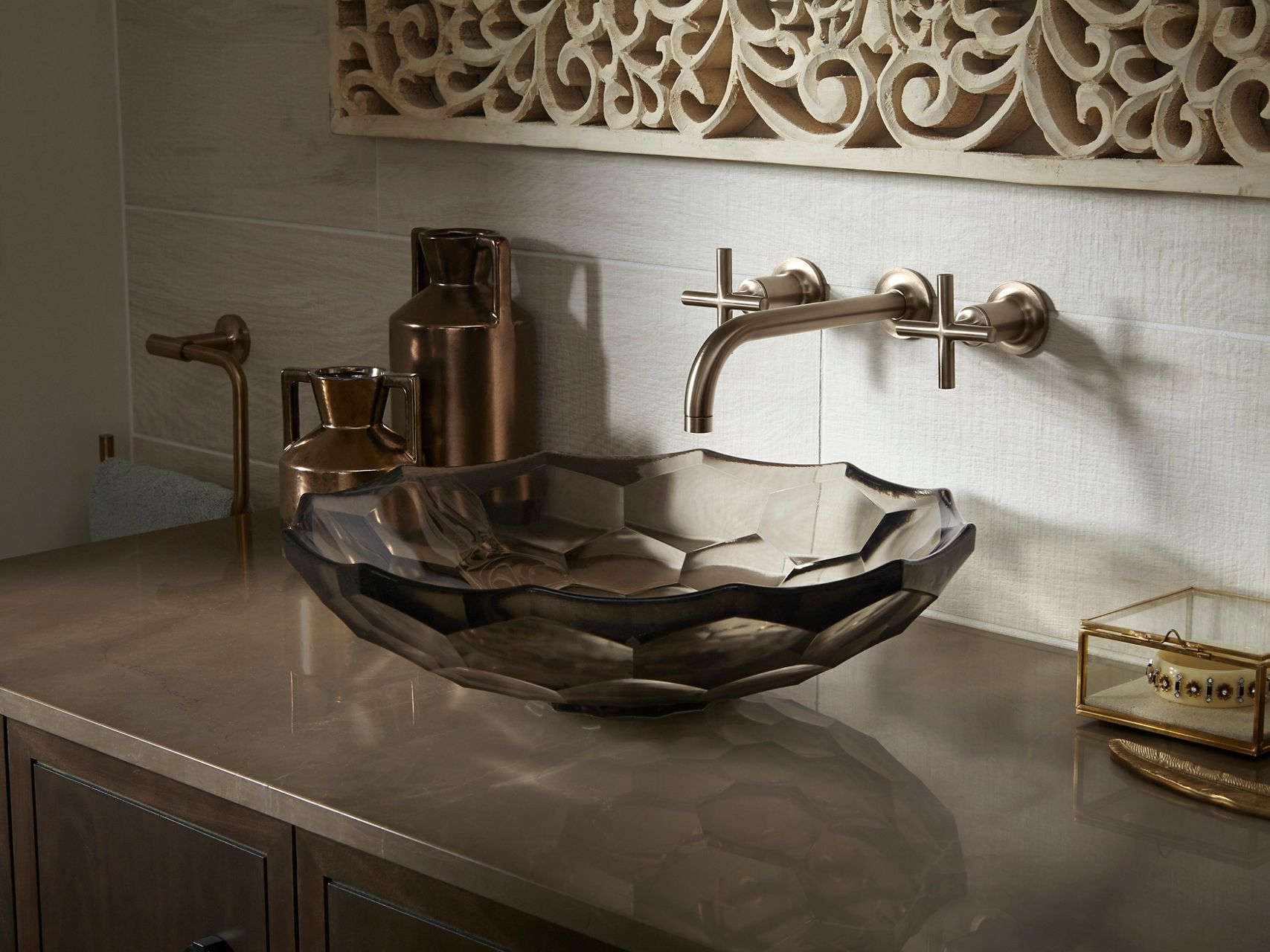 Un meuble-lavabo de salle de bain maussade avec des ombres fortes, des finis en bronze brossé et un lavabo en surface en verre à facettes dans une teinte fumée.