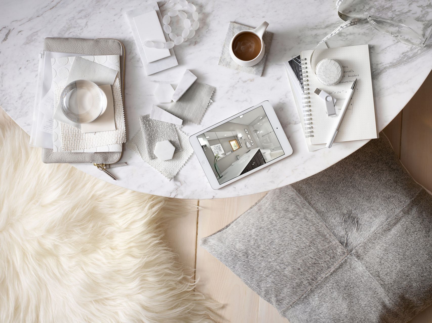 Overhead view of marble tabletop with tablet and bathroom design on screen, neautral tile and fabric samples, and coffee mug on a coaster.