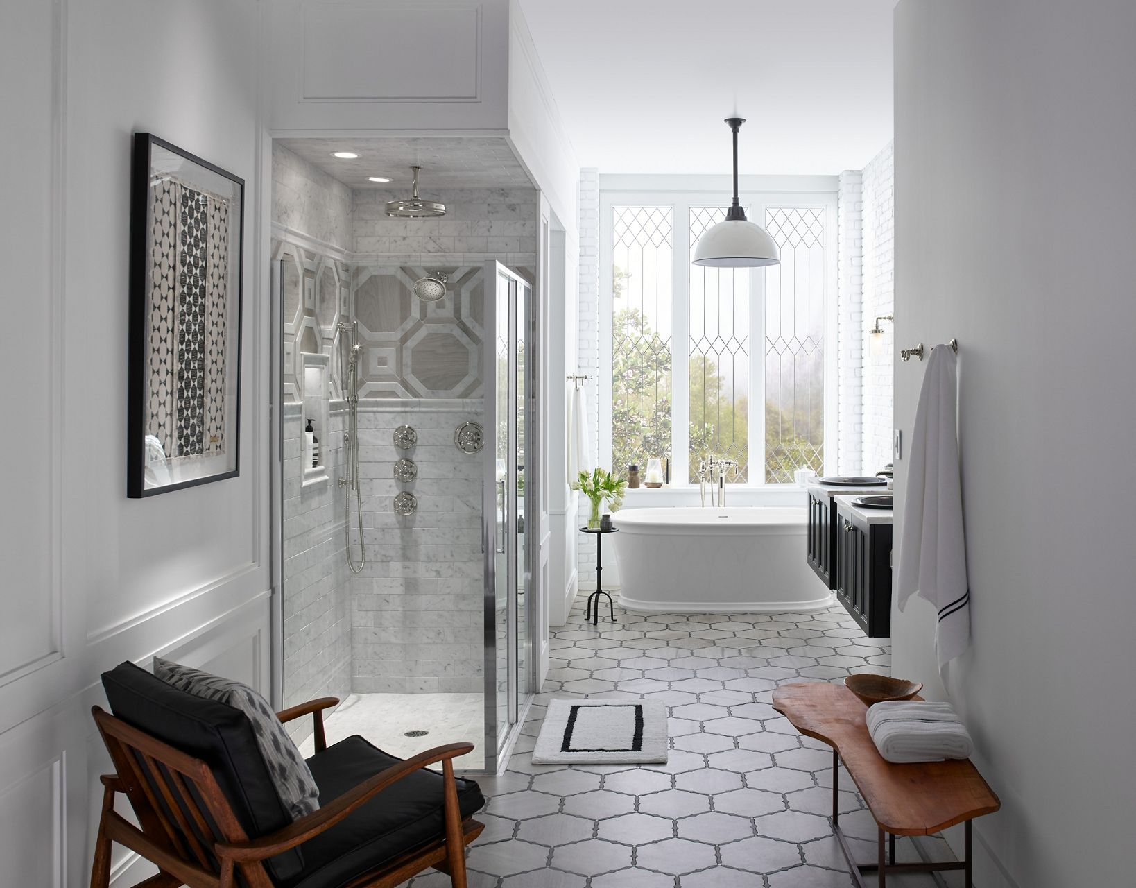 Une grande salle de bains avec une douche vitrée sur la gauche, une baignoire autoportante sous une fenêtre en verre au centre, et un meuble-lavabo double sur la droite.