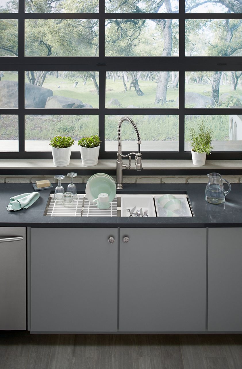 A stainless steel Prolific workstation sink with two built-in slotted racks holding drying dishes and two other built-in buckets being used to wash dishes.