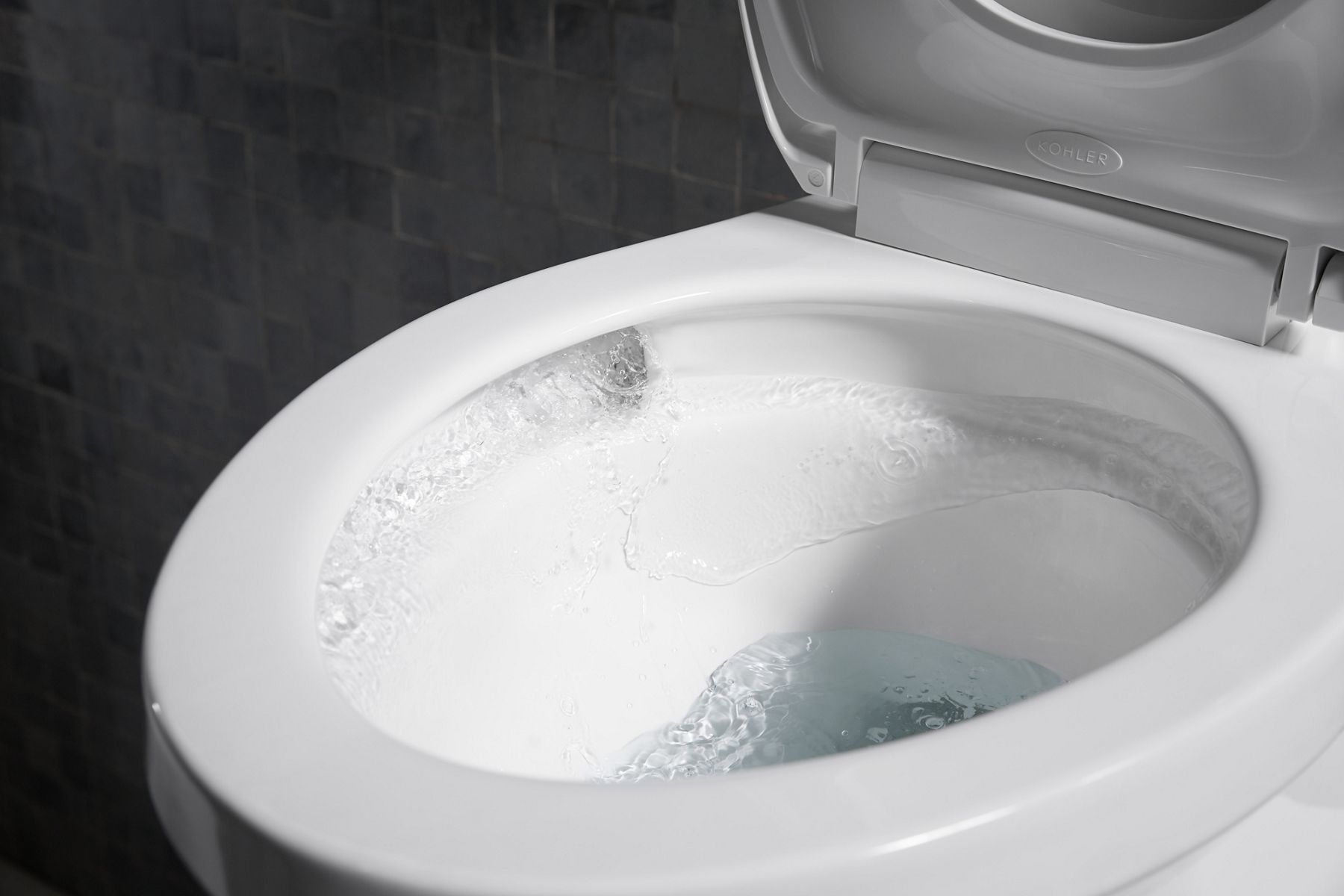 A white KOHLER Corbelle toilet, open with water swirling in 360 degrees around the entire bowl.