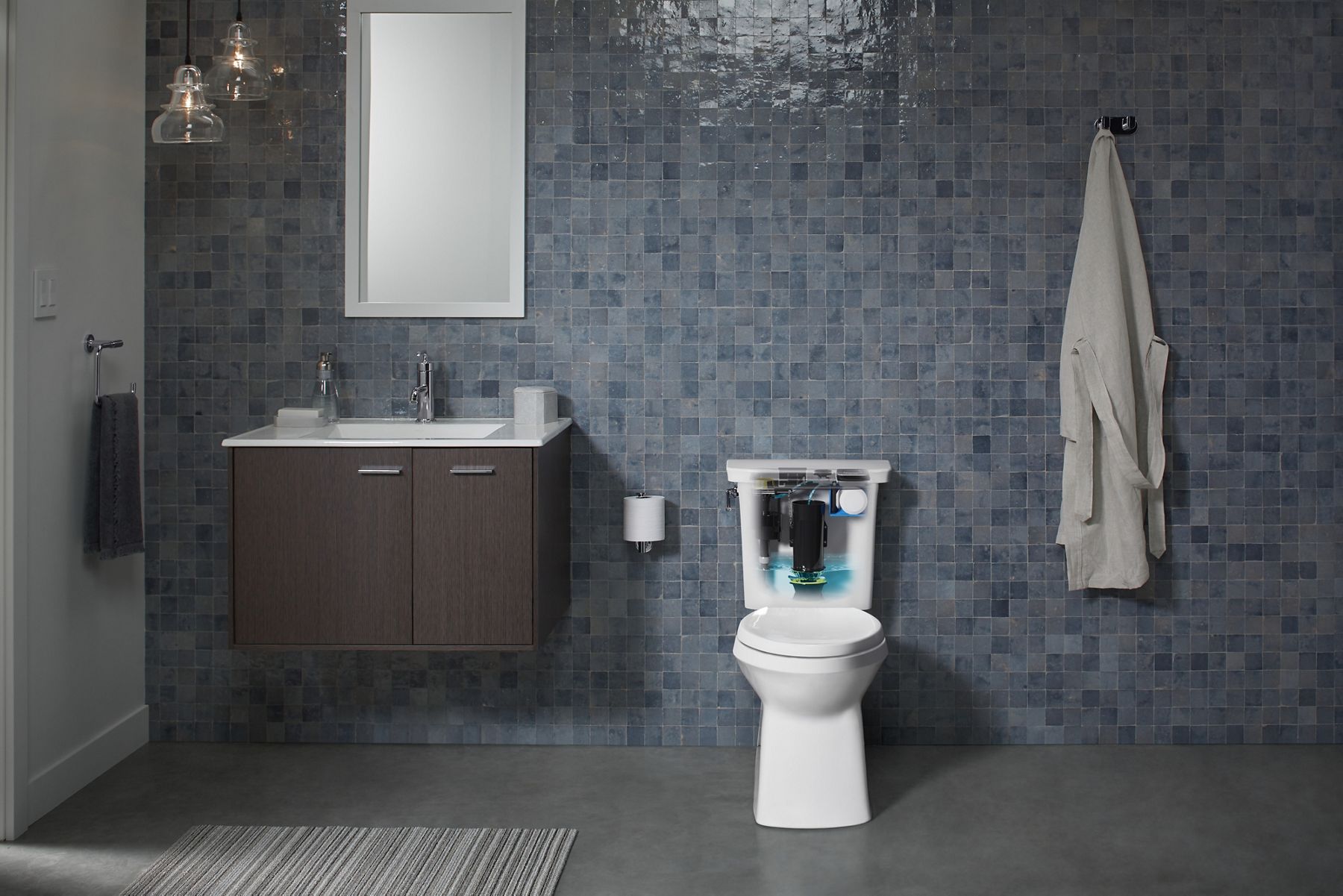 A green tiled bathroom with a white KOHLER Corbelle toilet with the tank cutaway to show the AquaPiston canister with Revolution 360 swirl flush technology components.