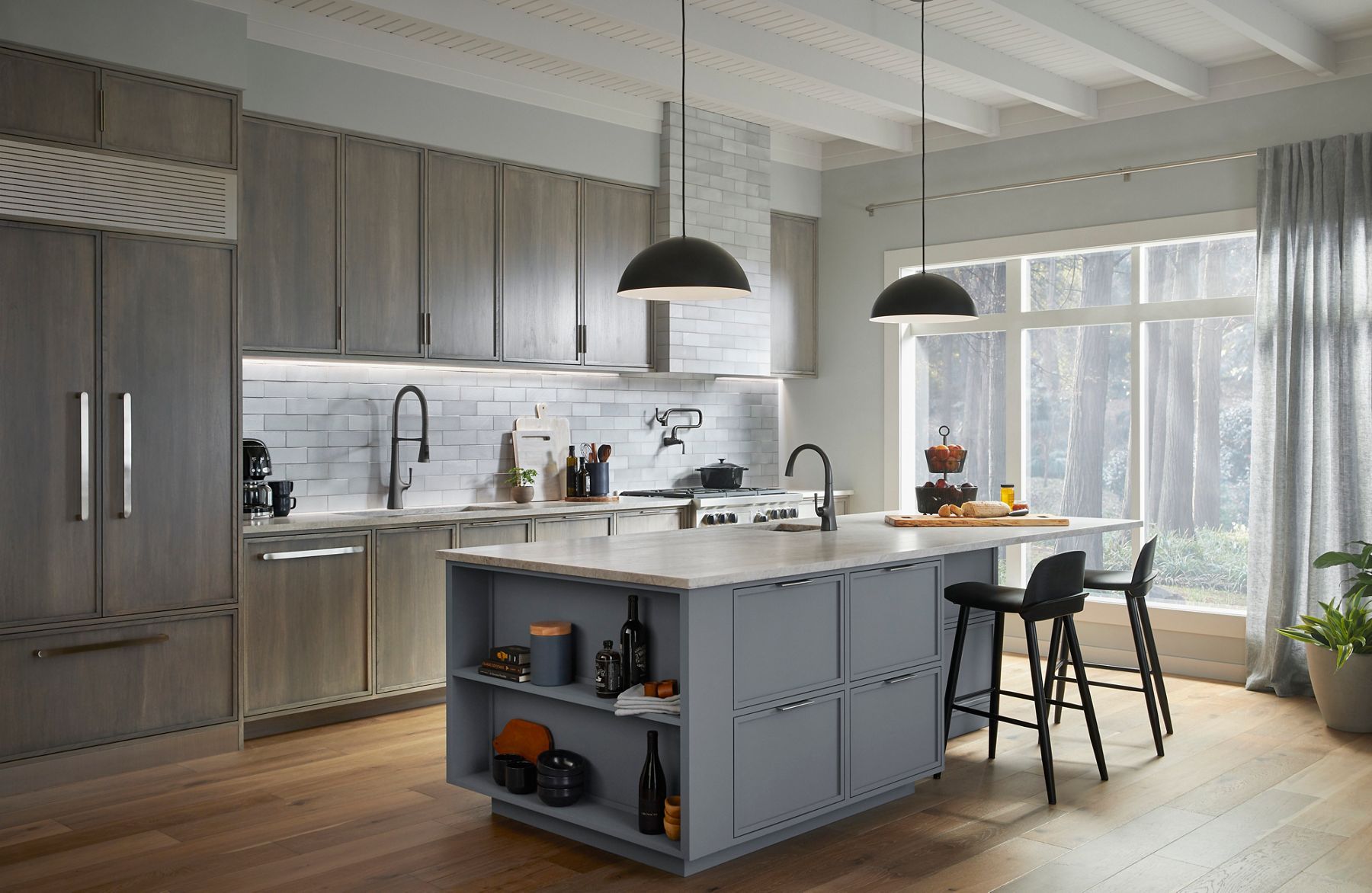 Kitchen with blue-gray kitchen island, island sink, counter sink and faucet, neutral cabintrey, light fixtures, kitchen range with pot filler, and white tile wall.