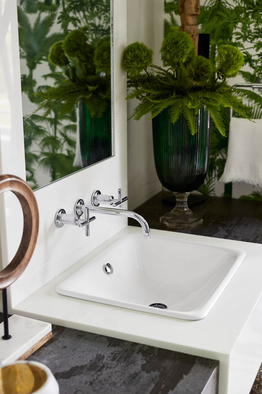 A rectangular white drop in sink in a white coutner top with a chrome wall-mount widespreawd faucet.