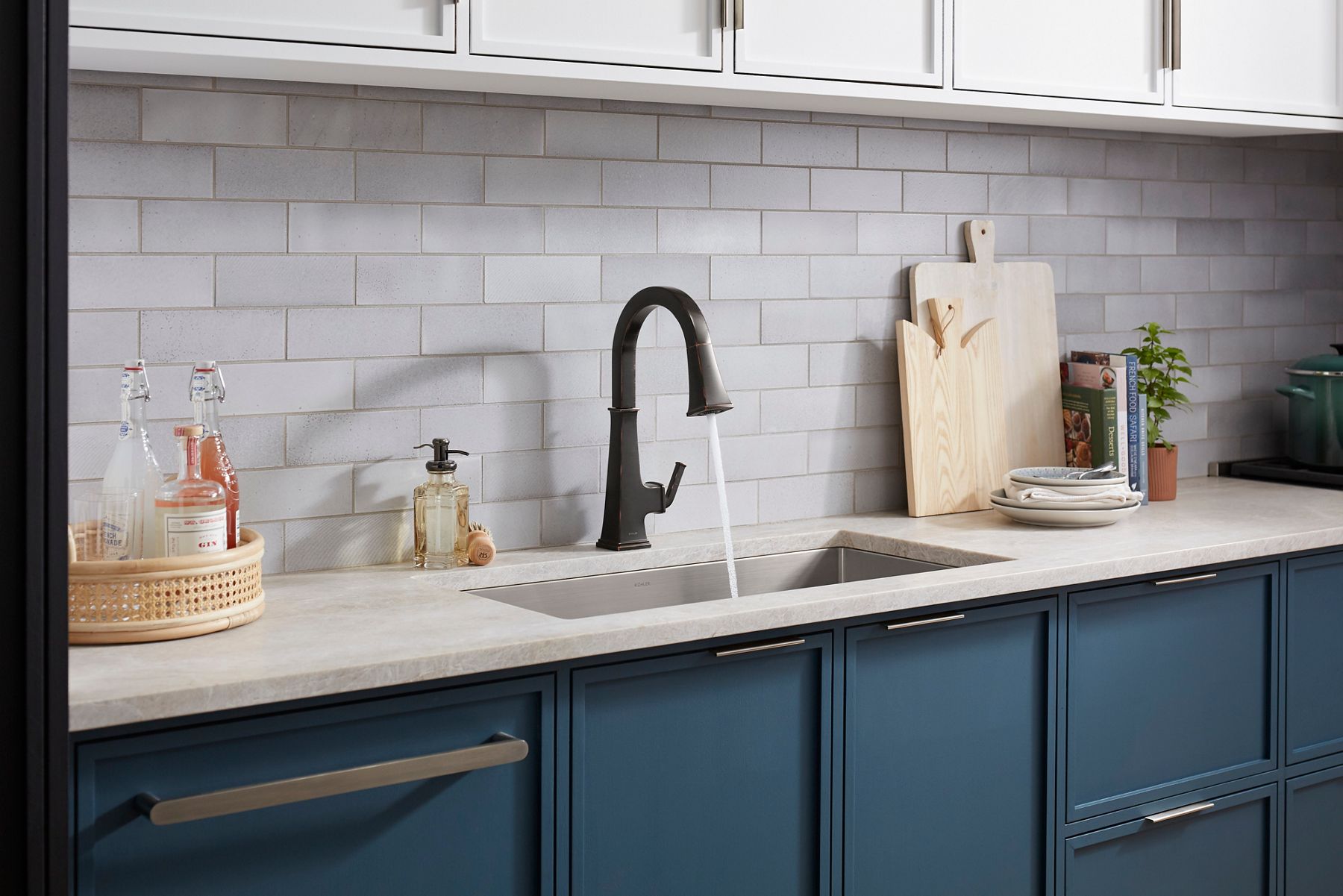A matte black kitchen facuet pouring water into an undermount stainless steel sink with a light gray tile backsplash.