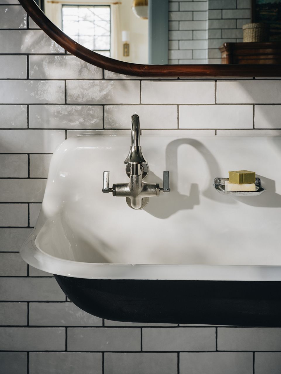 The left side of a large trough style cast iron sink focusing on the faucet and soap dish.