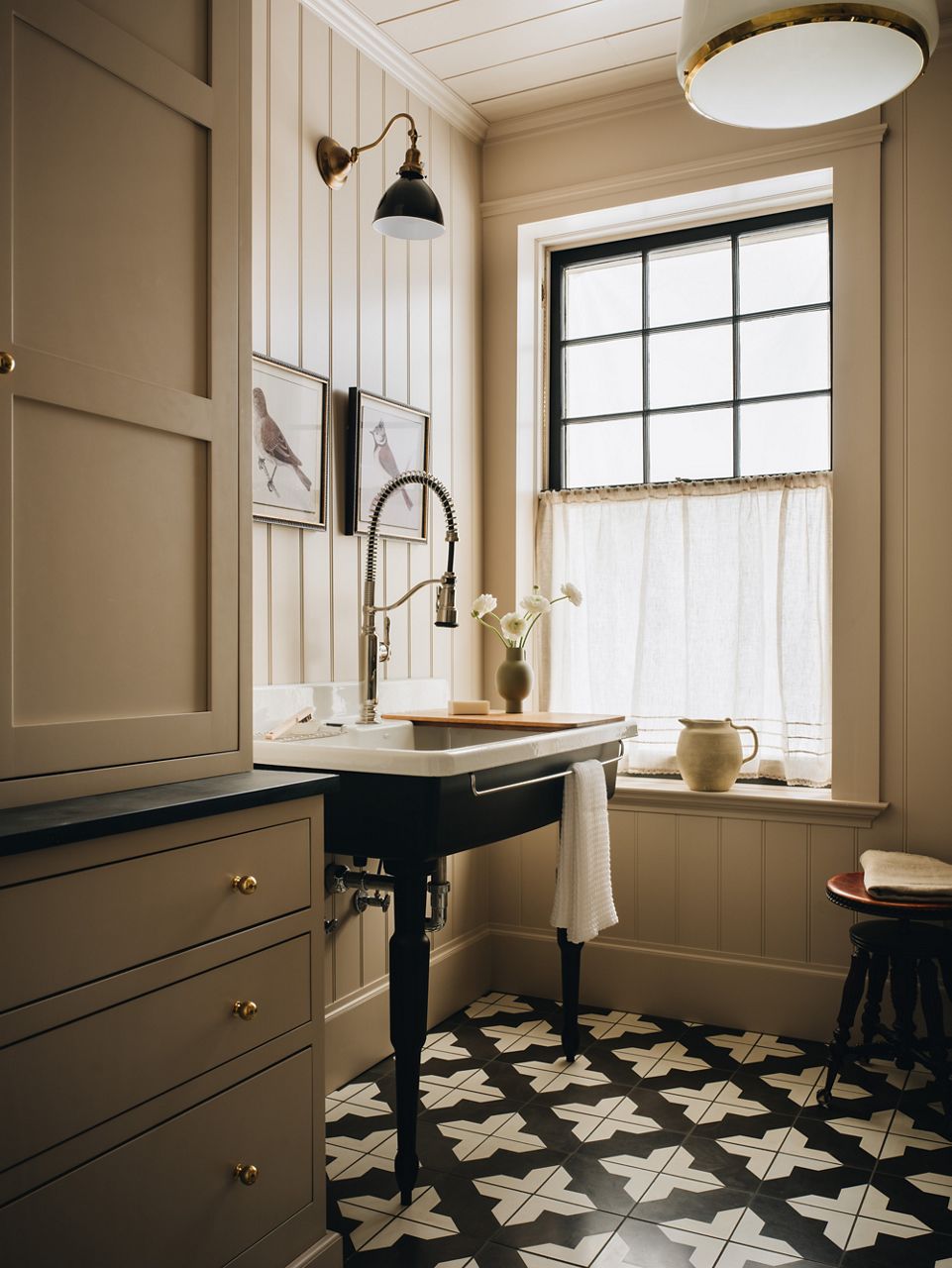A light and bright laundry room with a farmhouse wall mount sink on legs installed between a window and cabinets.