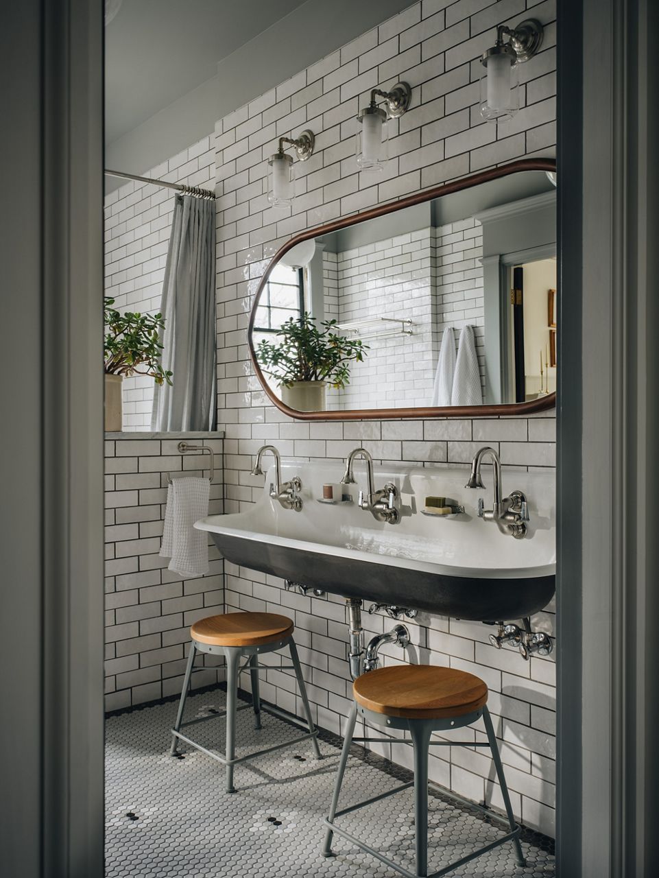 A light and bright bathroom with a large trough cast iron sink with three faucets installed on a wall with white subway tile.