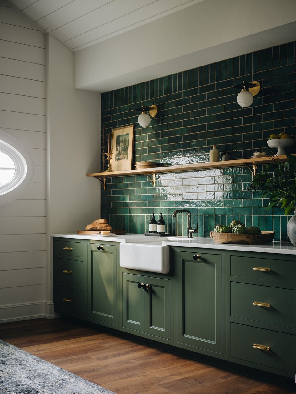 A kitchen space with green cabinets, white quartz countertops and an apron front white kitchen sink made from cast iron material.