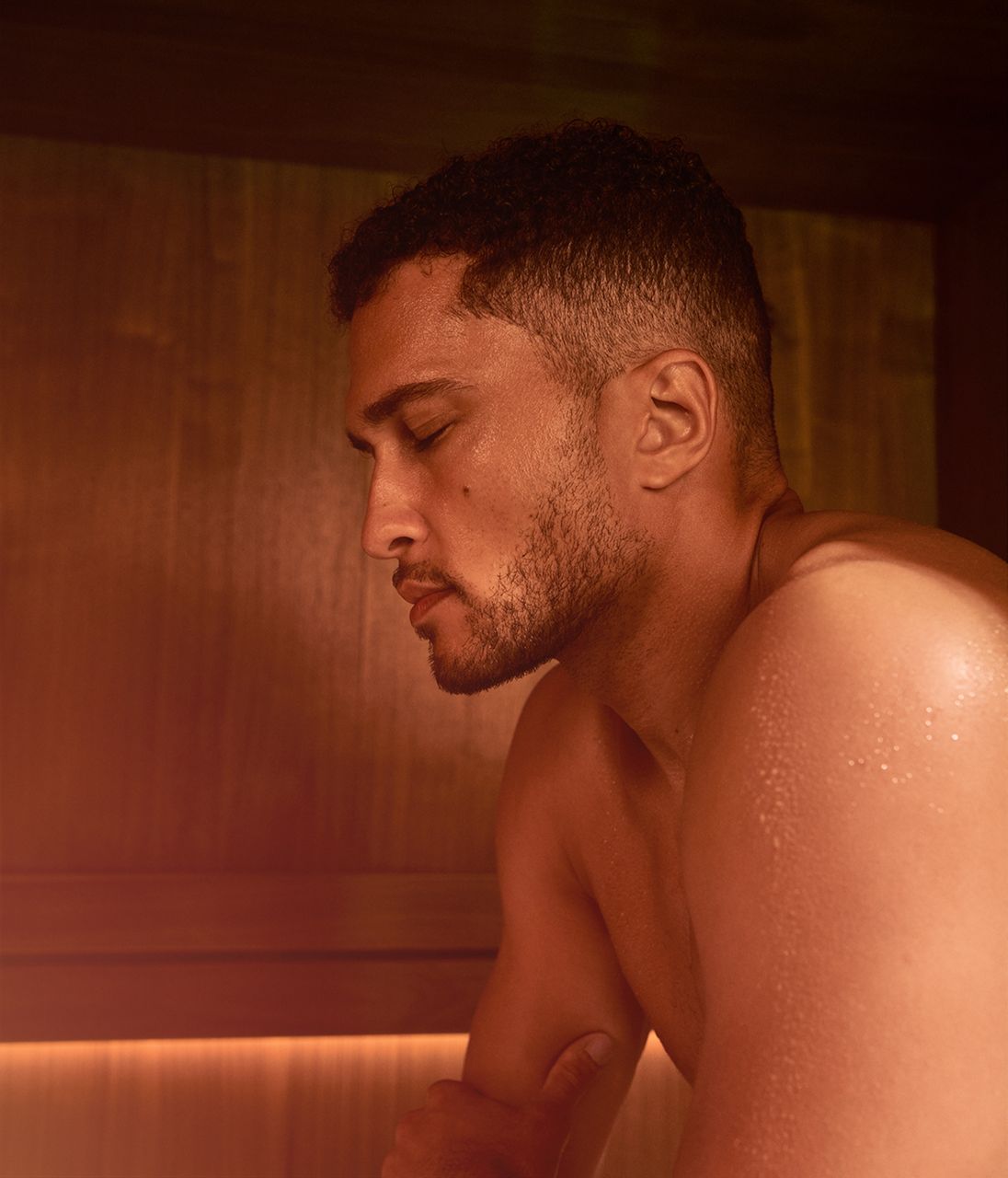 A man relaxing in a sauna with his eyes closed.